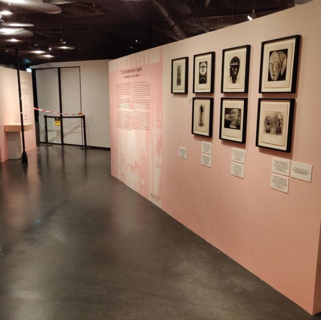 Cimaise rose avec photographies encadrées d'objets d'art africain et panneau de texte