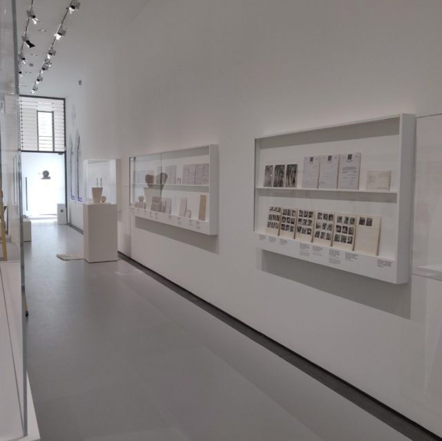 Couloir d'exposition avec vitrines murales de documents d'archives et céramiques