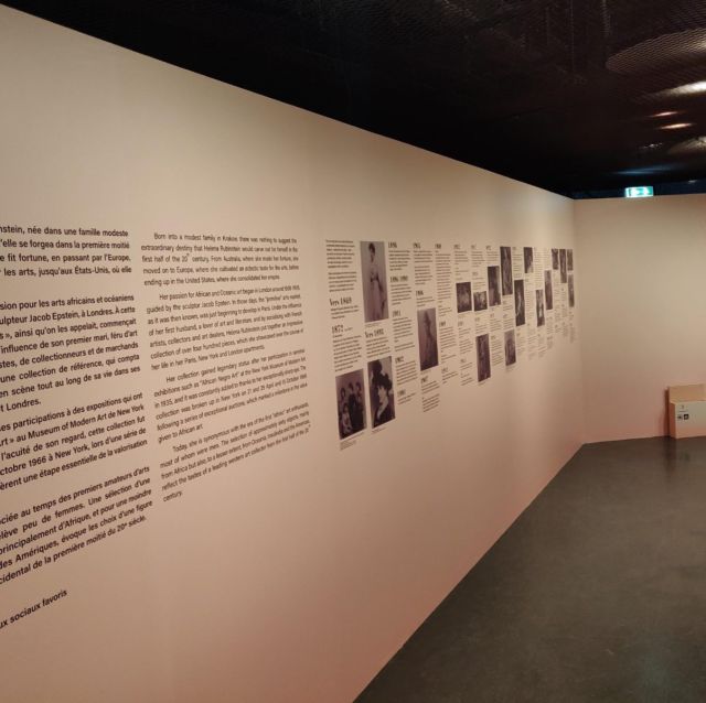 Mur d'exposition avec texte biographique bilingue et frise chronologique photographique