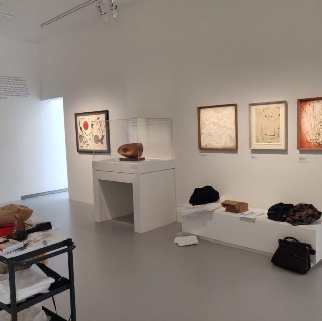 Salle d'exposition avec œuvres encadrées et sculpture sur socle vitré
