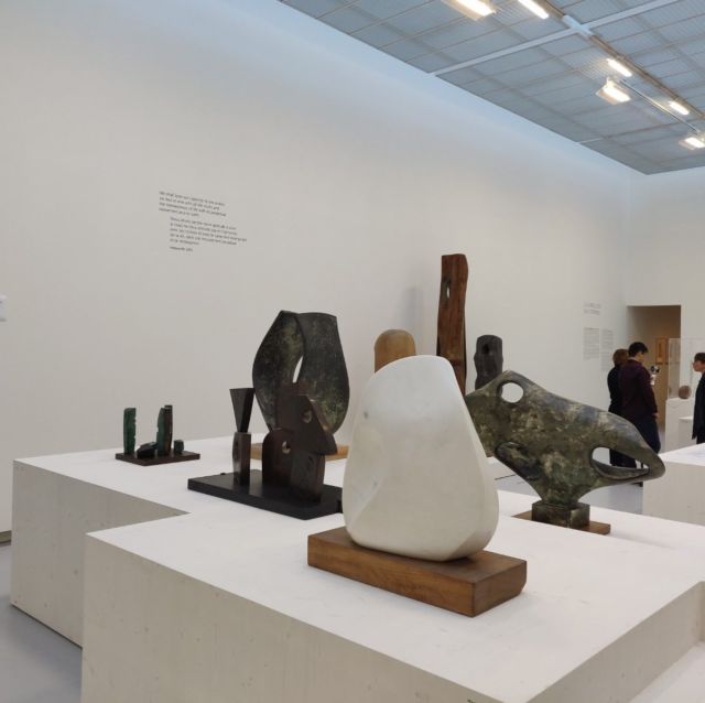 Salle d'exposition de sculptures modernes en pierre et bronze sur socles blancs, avec visiteurs